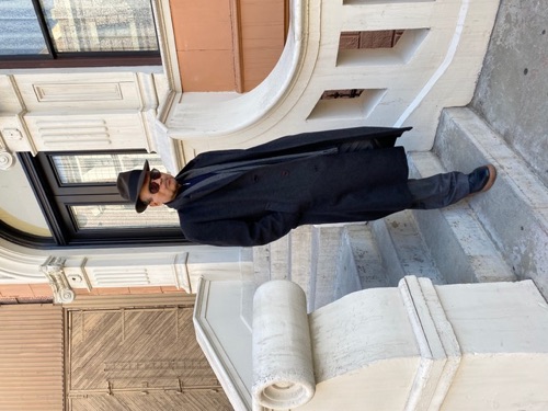 Joe Gironda in overcoat and fedora on a city stoop